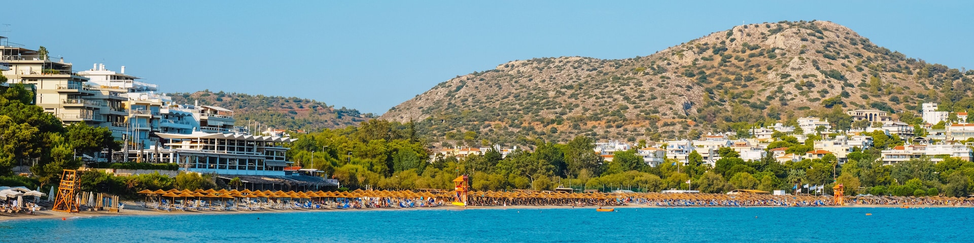 A coastal town with a beach, a mountain, and buildings along the shore.