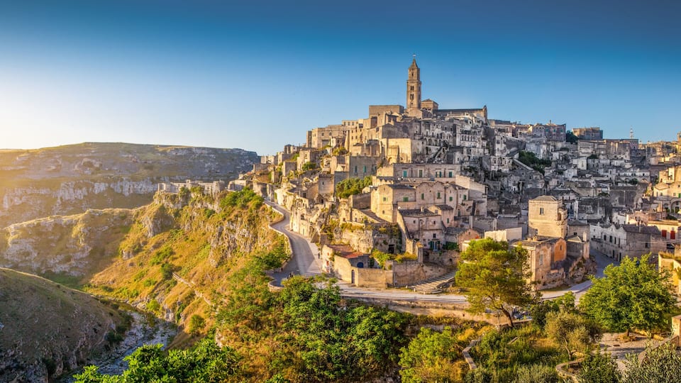 A historic town perched on a hillside with a prominent church tower, terraced buildings, and a winding road.