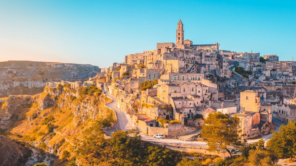 A historic town perched on a hillside with a prominent tower, winding roads, and rugged terrain.