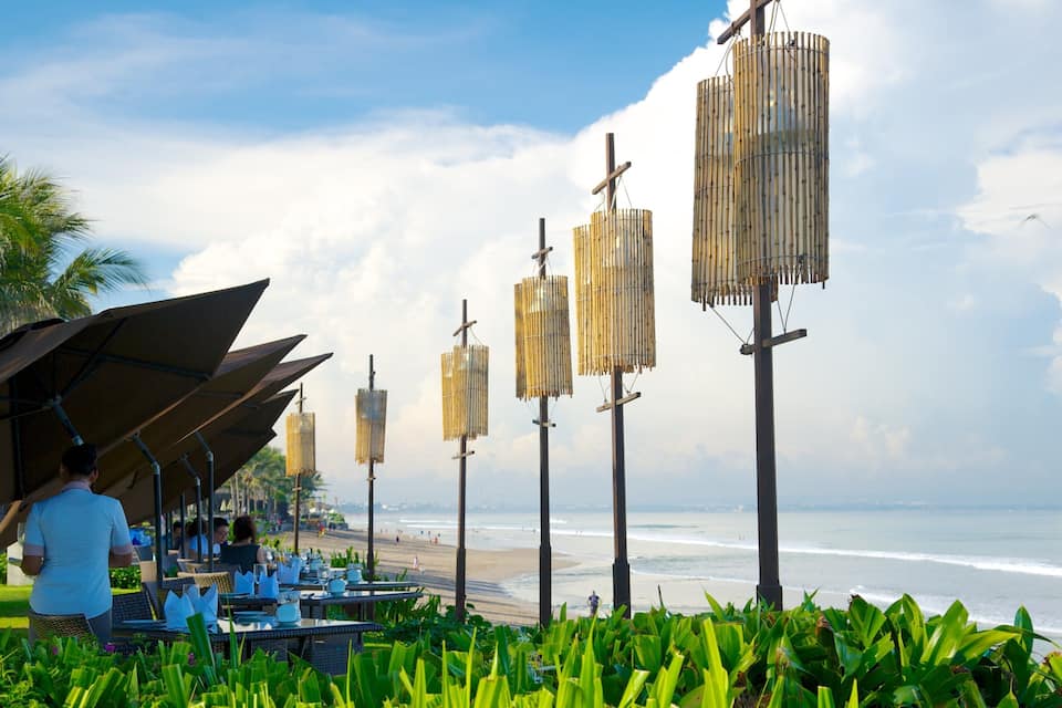 Un restaurant situé en bord de mer, avec une terrasse, des palmiers et une vue sur l’océan.
