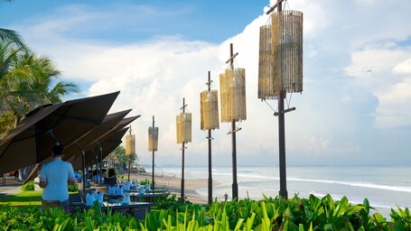 Ein Restaurant am Strand mit Terrassensitzgelegenheiten, Palmen und Meerblick.