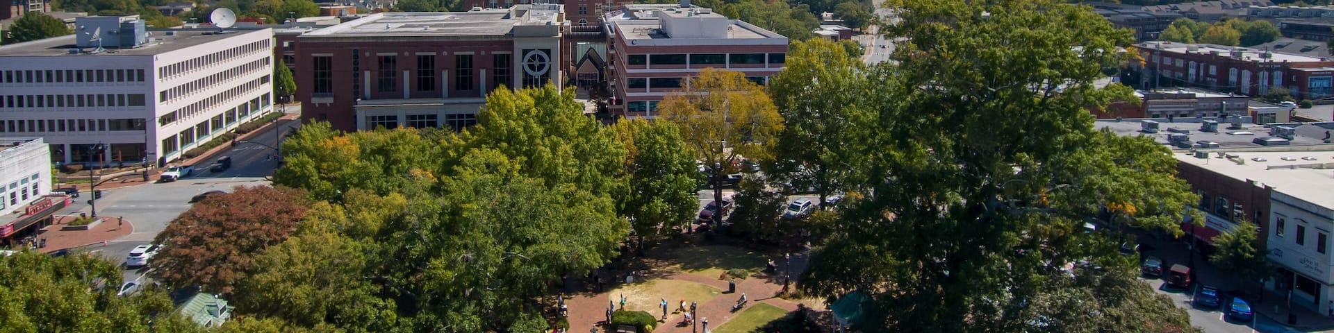 an aerial shot of a gorgeous autumn landscape at the Marietta Square with a water fountain surrounded by lush green trees and autumn colored trees with buildings at sunset in Marietta Georgia USA
