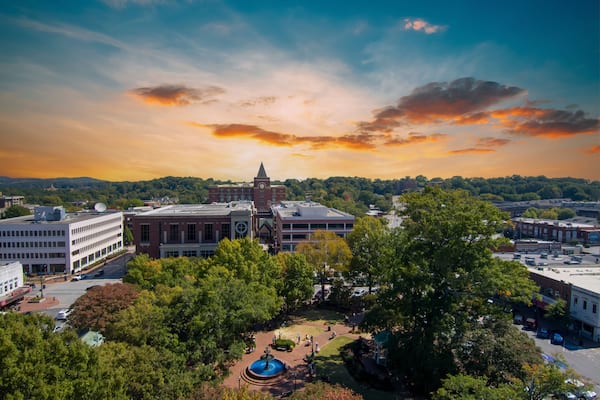 an aerial shot of a gorgeous autumn landscape at the Marietta Square with a water fountain surrounded by lush green trees and autumn colored trees with buildings at sunset in Marietta Georgia USA