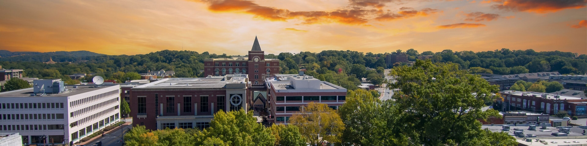an aerial shot of a gorgeous autumn landscape at the Marietta Square with a water fountain surrounded by lush green trees and autumn colored trees with buildings at sunset in Marietta Georgia USA