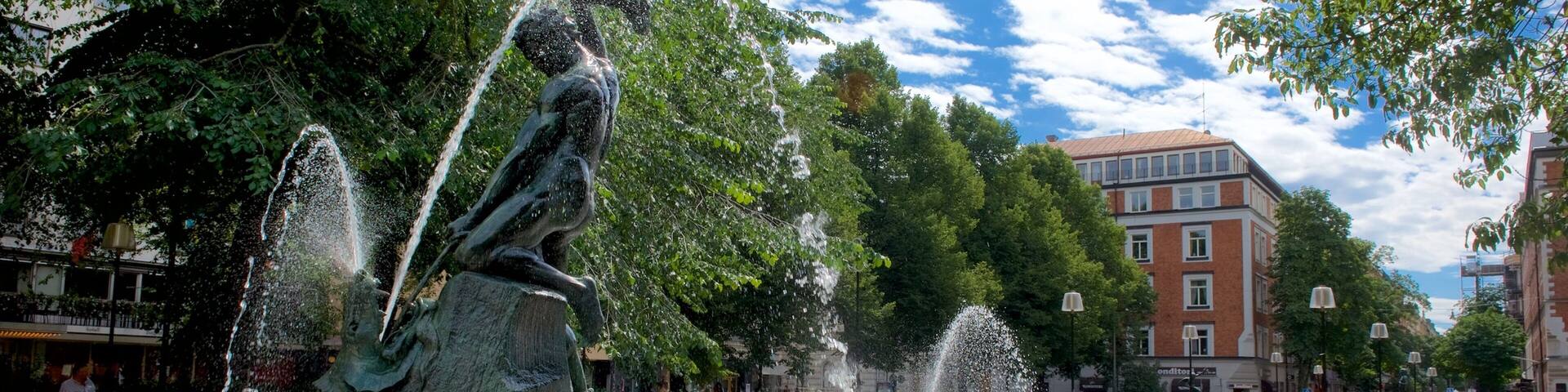 A public fountain with water jets, surrounded by trees and buildings.