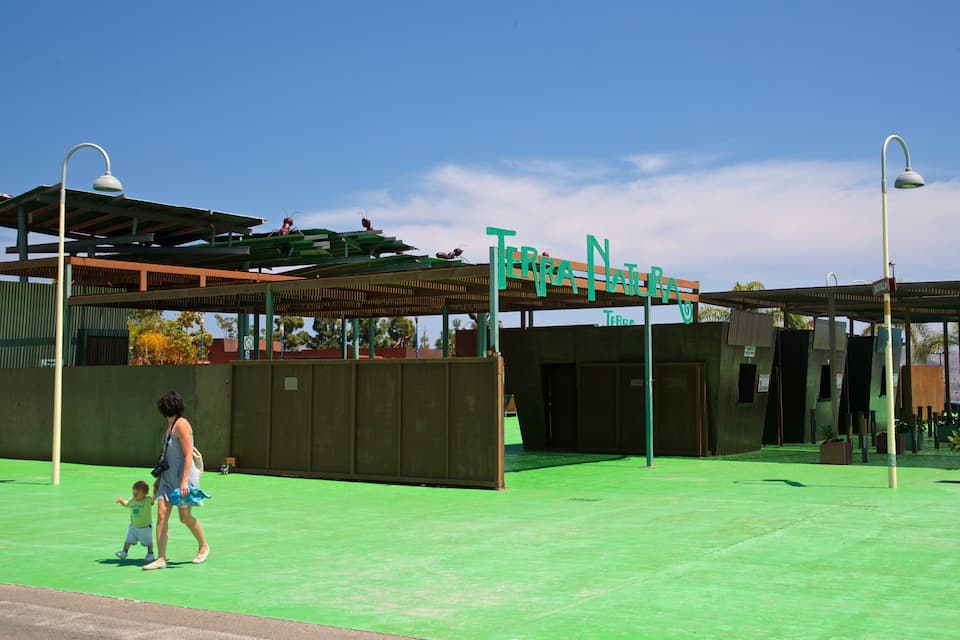 Een gebied met kunstgras, een bord met de tekst 'TERRA NATURA' en een overdekte constructie met een dak.