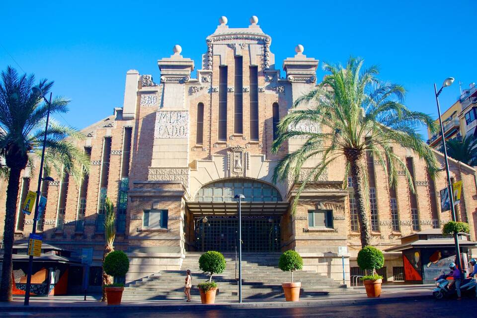 A historic building with a grand entrance, palm trees, and a clear blue sky.