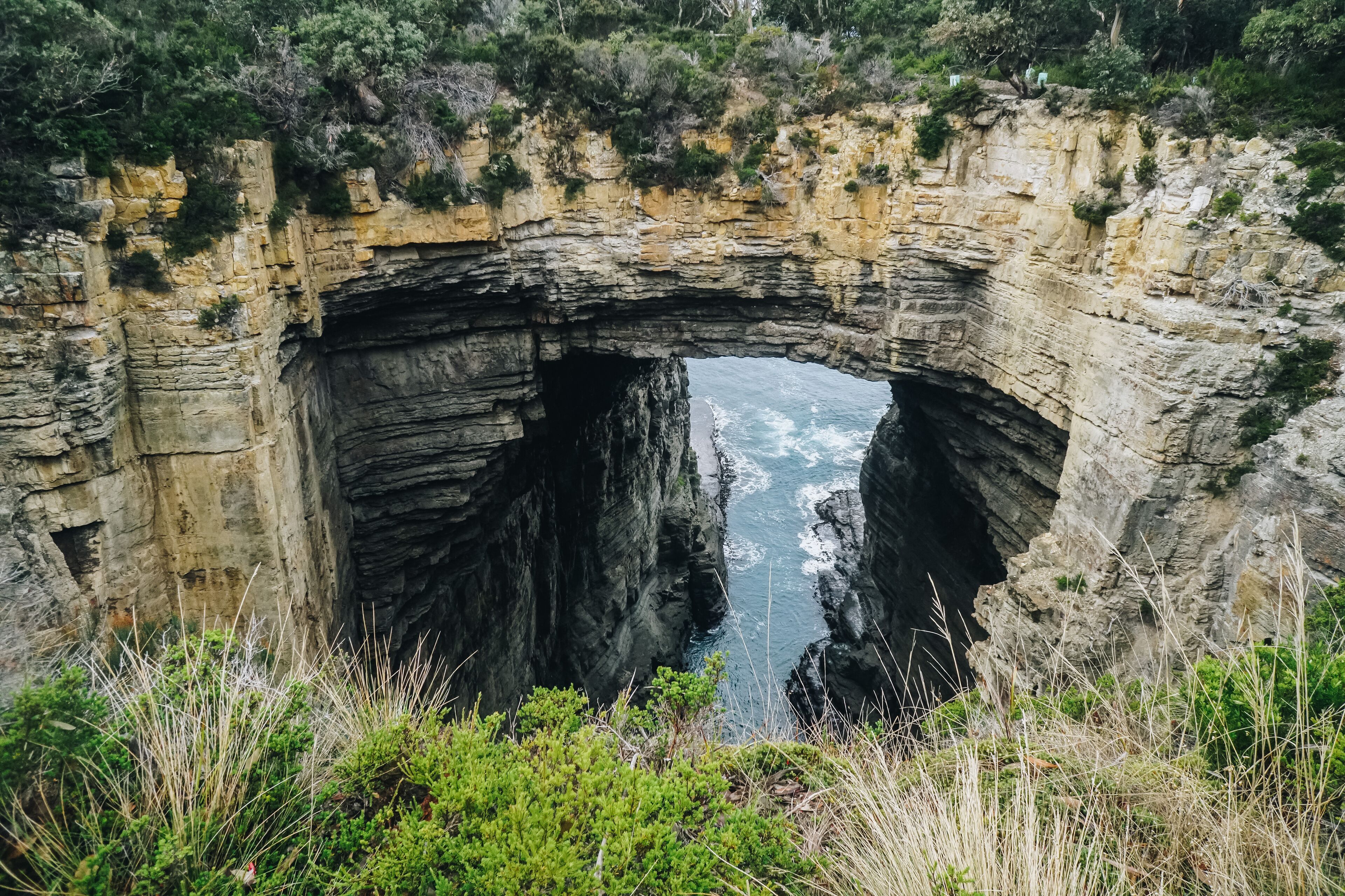 A natural rock arch formation with a river flowing through it.