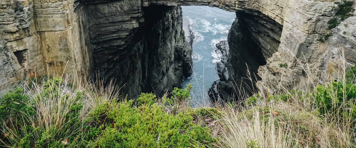 A natural rock arch formation with a river flowing through it.