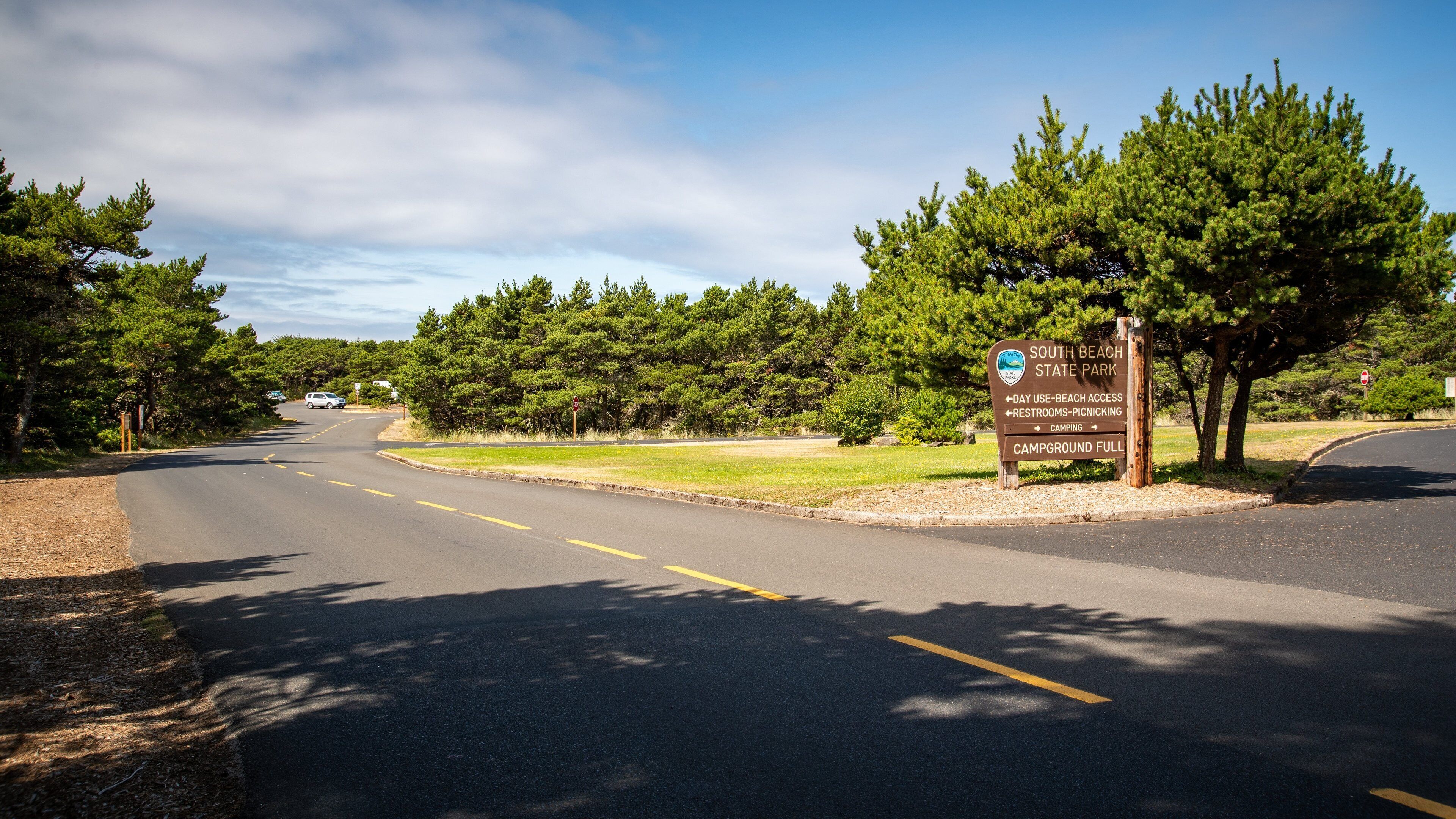 A road leading to South Beach State Park with a sign indicating day use beach access, restrooms, picnicking, and a full campground.