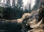 A natural hot spring surrounded by forested mountains.