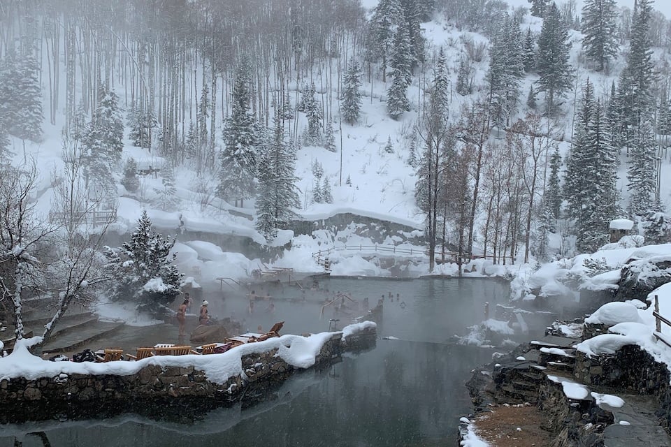 A snowy landscape with a river, trees, and a stone bridge.