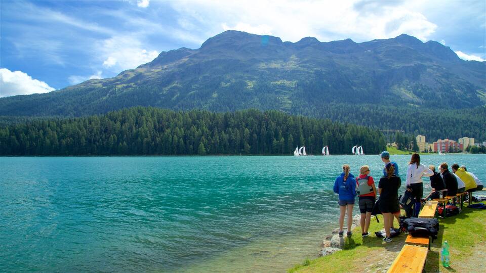 A lake with sailboats, a forested mountain, and people on the shore.