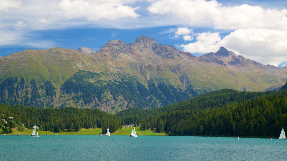A lake with sailboats, surrounded by forested hills and mountains.