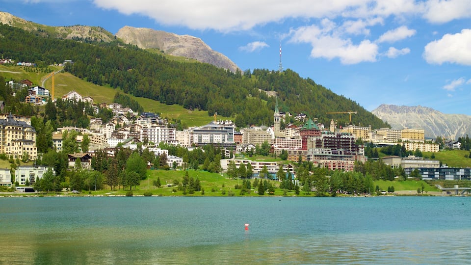 A lakeside town with buildings, a mountain, and a tower.