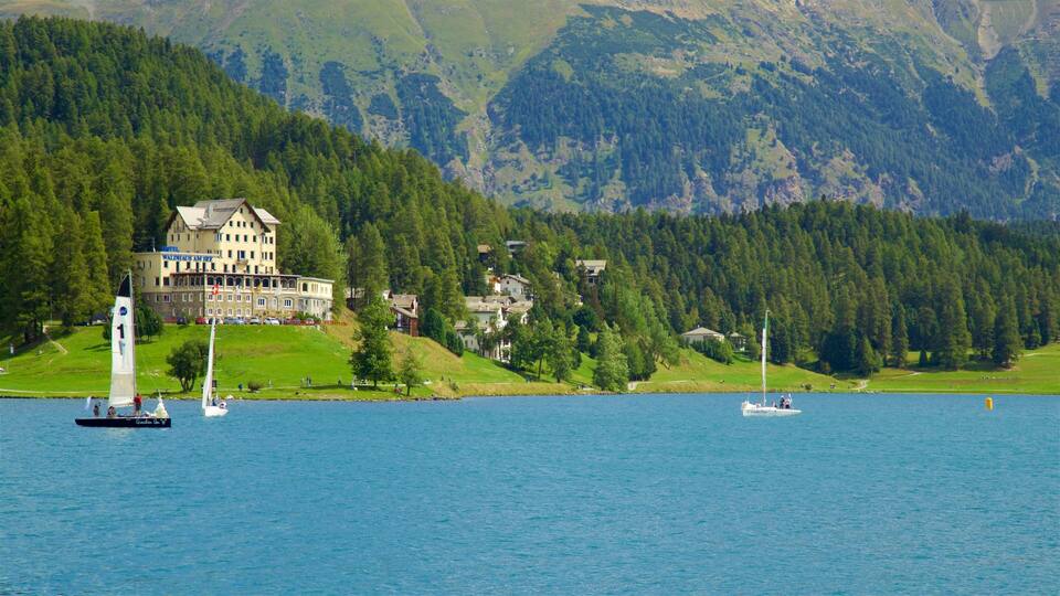 A lake with sailboats, a large house with a balcony, and forested mountains in the background.