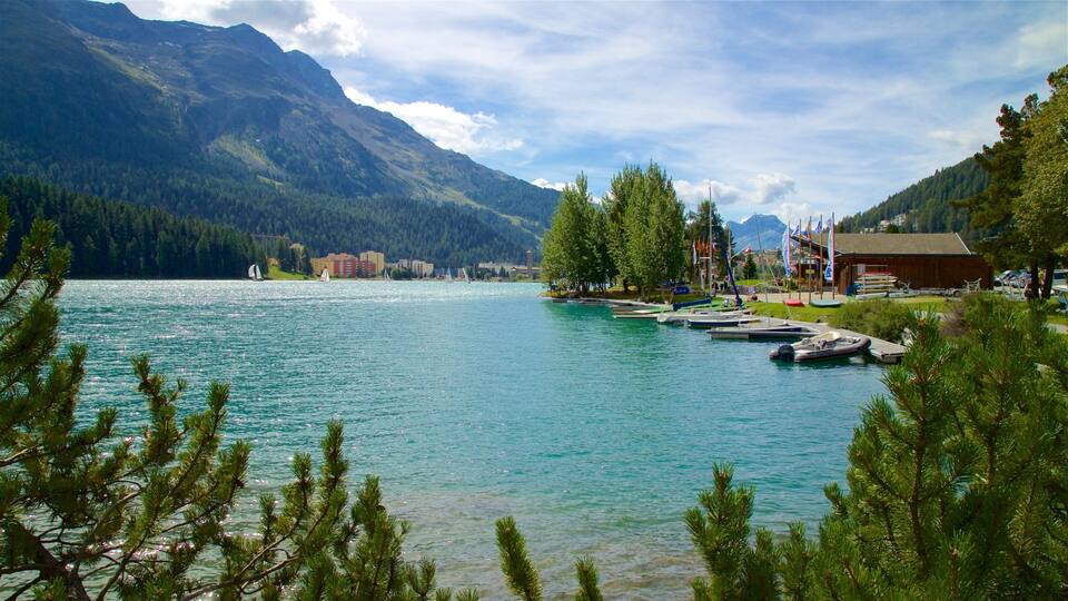 A lake with boats, a dock, mountains, and a building with flags.