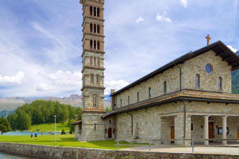 Una iglesia de piedra con un campanario alto y un paisaje montañoso de fondo.