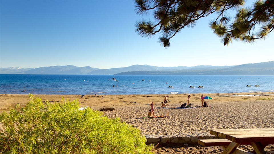 A beach with people sunbathing and swimming, a clear blue sky, and mountains in the distance.