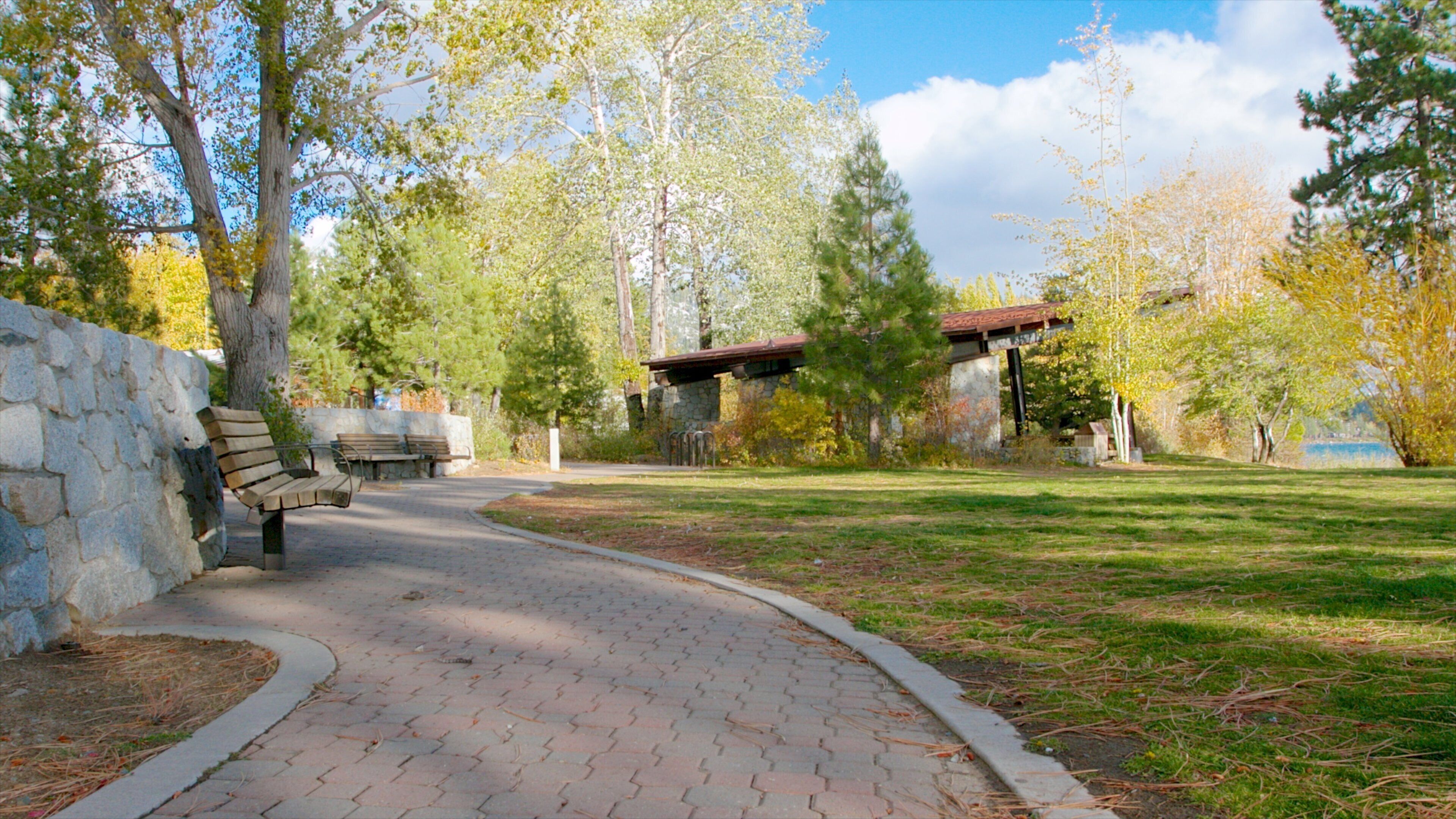 A park with a paved walkway, benches, stone walls, and trees.