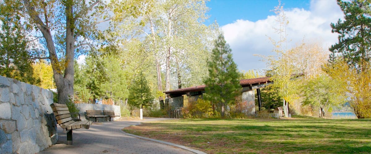 A park with a paved walkway, benches, stone walls, and trees.