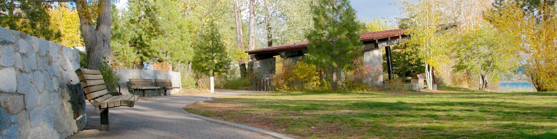 A park with a paved walkway, benches, stone walls, and trees.