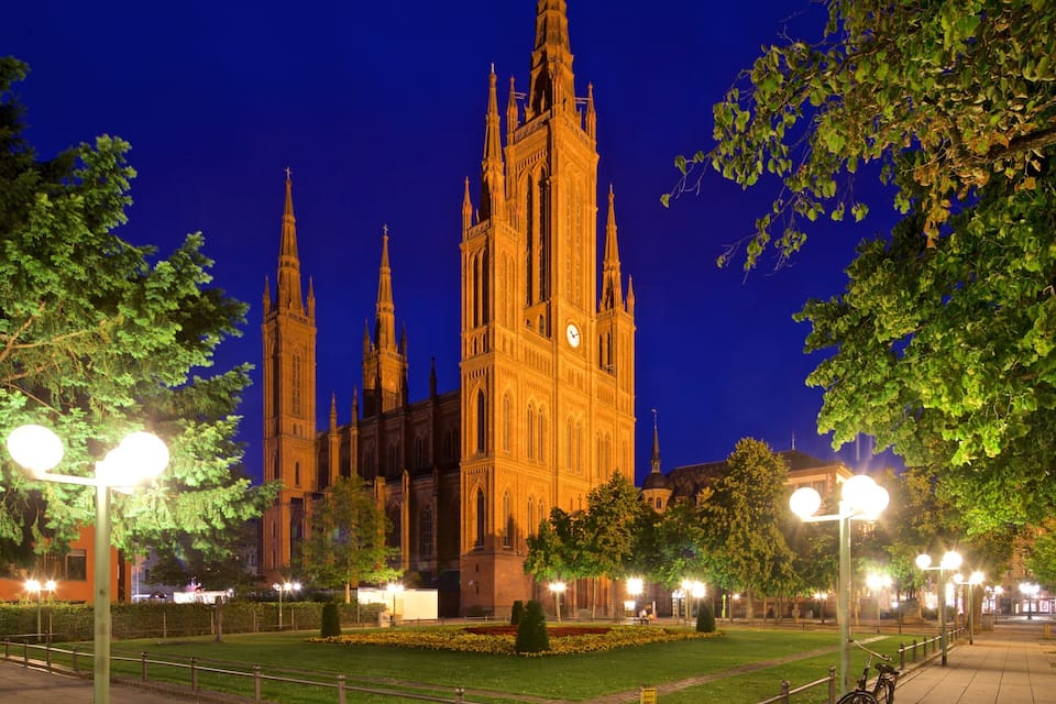 A historic cathedral with tall spires, surrounded by well-lit trees and a paved walkway.