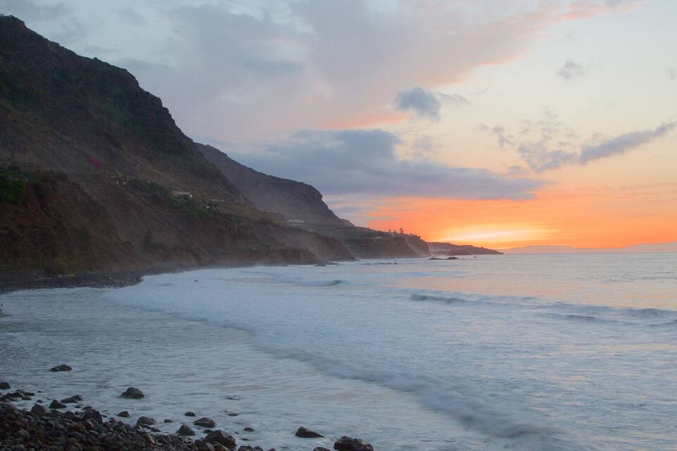 A coastal landscape with a rocky shoreline, waves, and a sunset over the ocean.