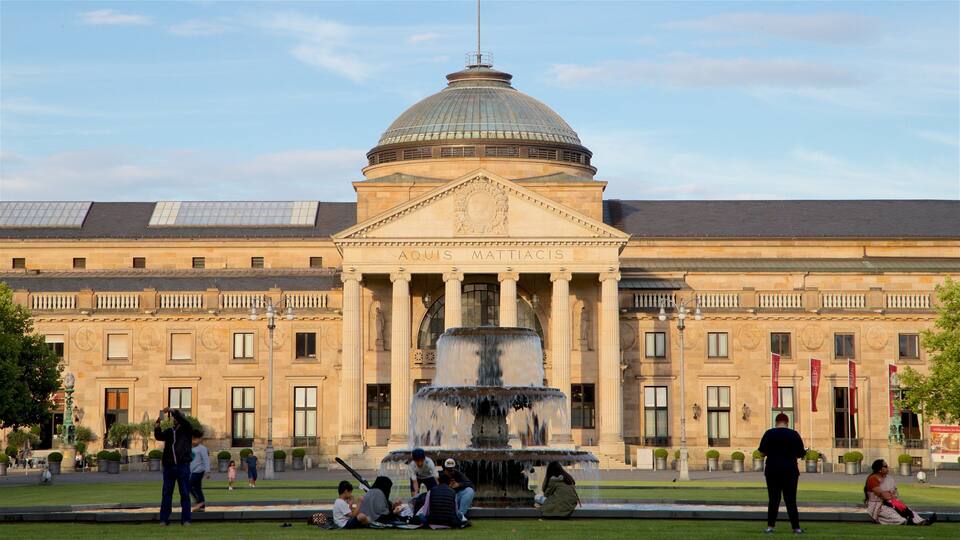 A historic building with a large dome and columns, a fountain in front, and people sitting and walking around.