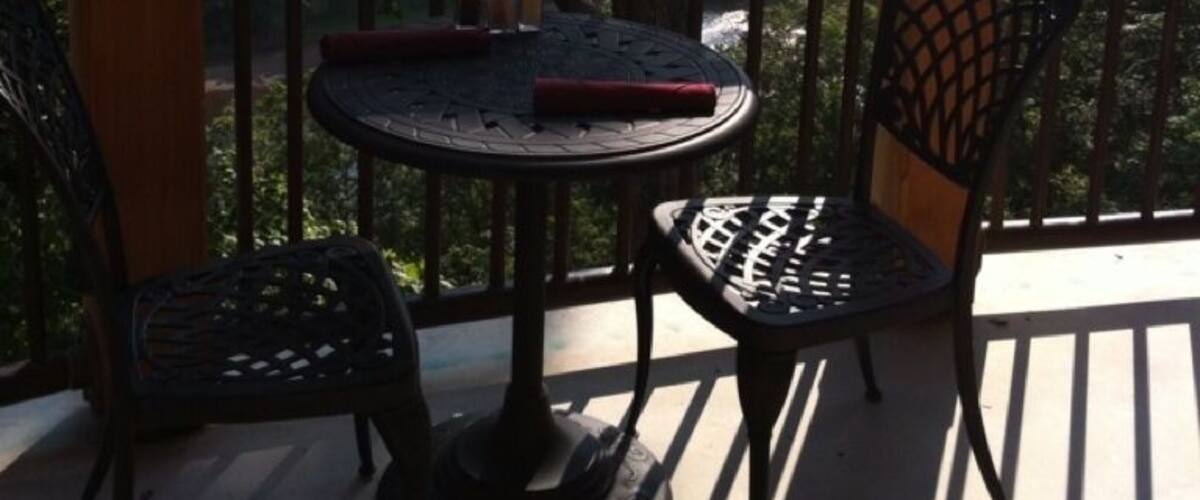 A wooden deck with a table and chairs, overlooking a scenic landscape with trees and distant buildings.