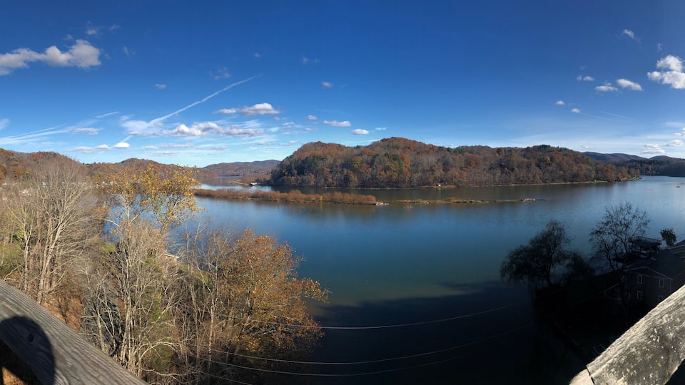 A wooden bridge over a calm lake surrounded by autumn-colored trees and hills.