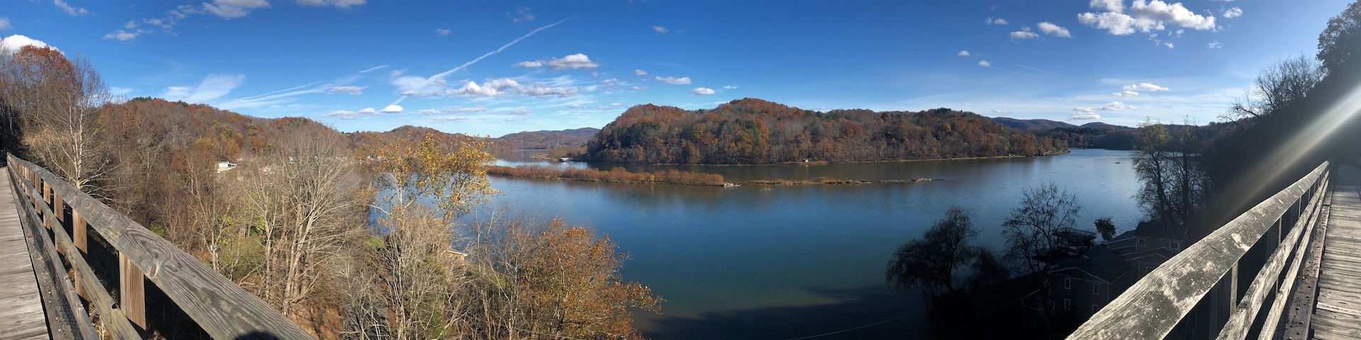 A wooden bridge over a calm lake surrounded by autumn-colored trees and hills.