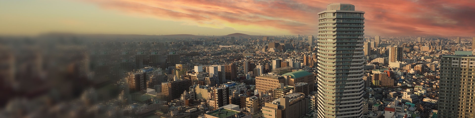 Paisagem urbana com um edifício alto em destaque, área urbana densa e céu ao pôr do sol.