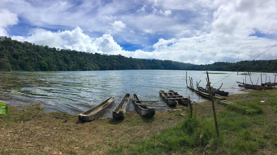 A lake with several wooden boats on the shore, surrounded by a forested landscape.