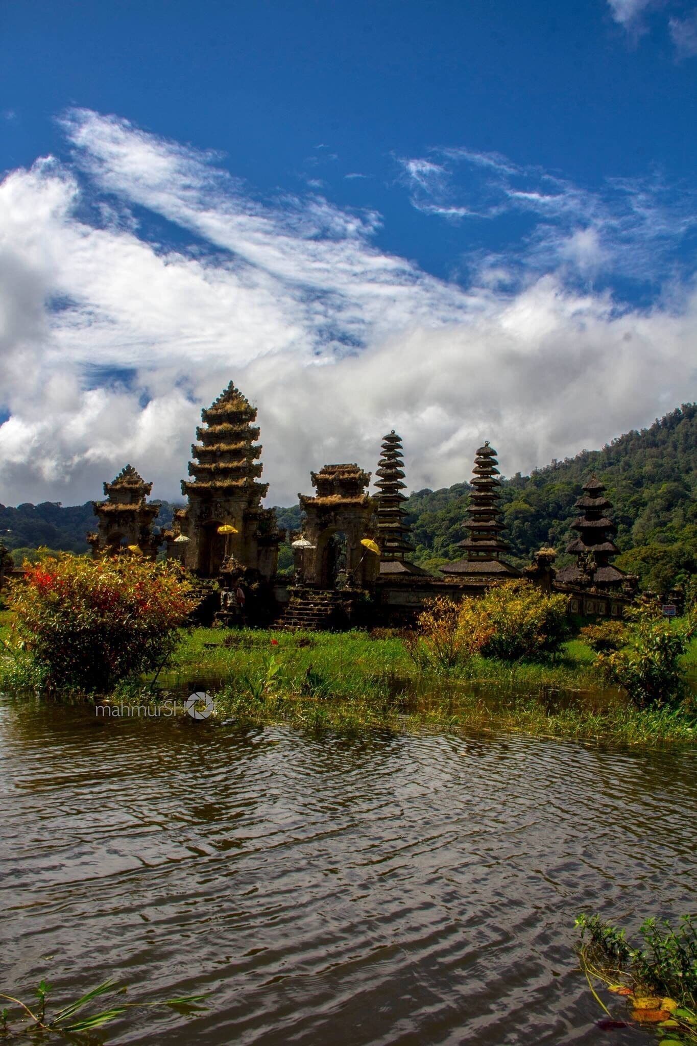 Un complejo de templos con pagodas escalonadas rodeado de abundante vegetación y una masa de agua.