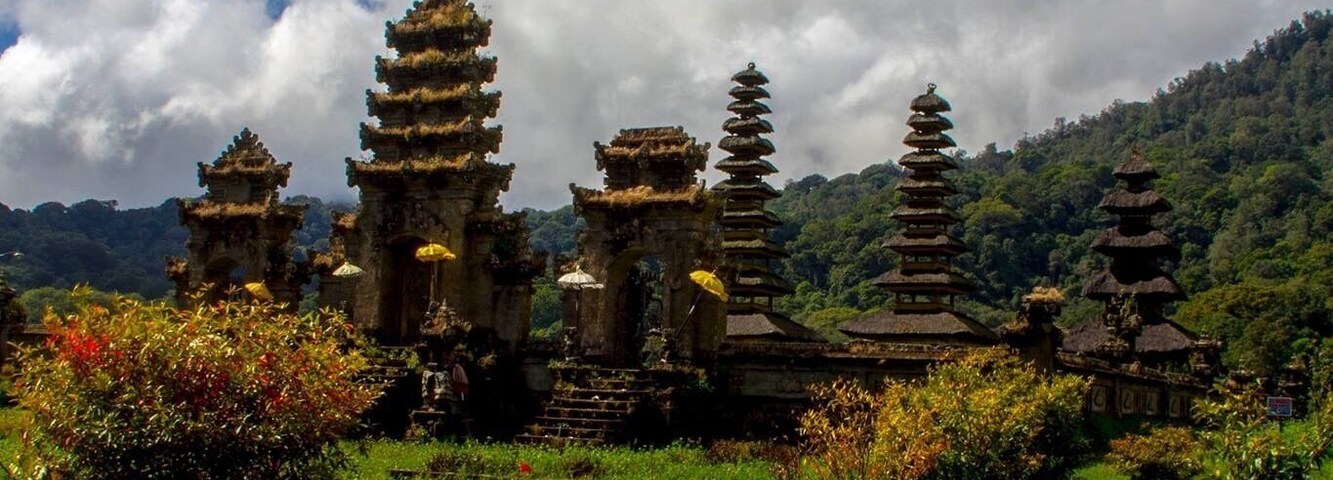 Un complejo de templos con pagodas escalonadas rodeado de abundante vegetación y una masa de agua.