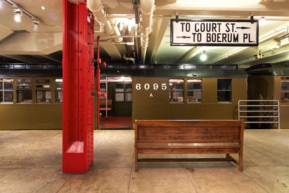 Eine U-Bahn-Station mit einer Bank, einer roten Säule und einem Schild, das die Richtung zu Court St. und Boerum Pl. anzeigt.