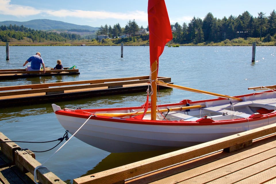 A small red and white sailboat docked at a wooden pier with a forested mountain range in the background.