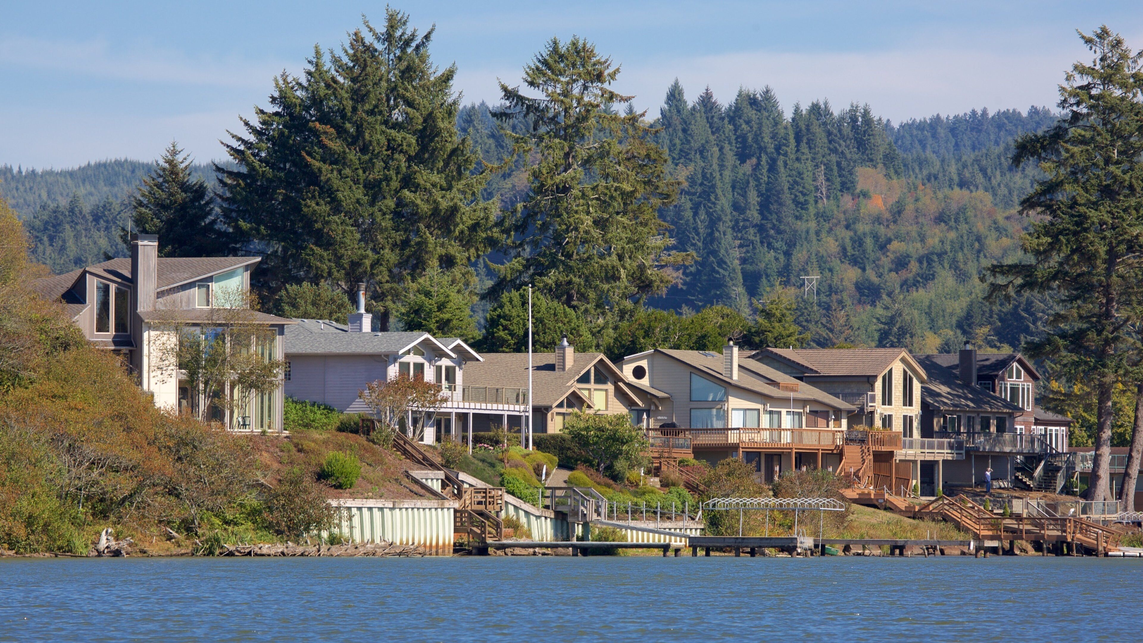 A waterfront residential area with houses, a dock, and a forested hillside.