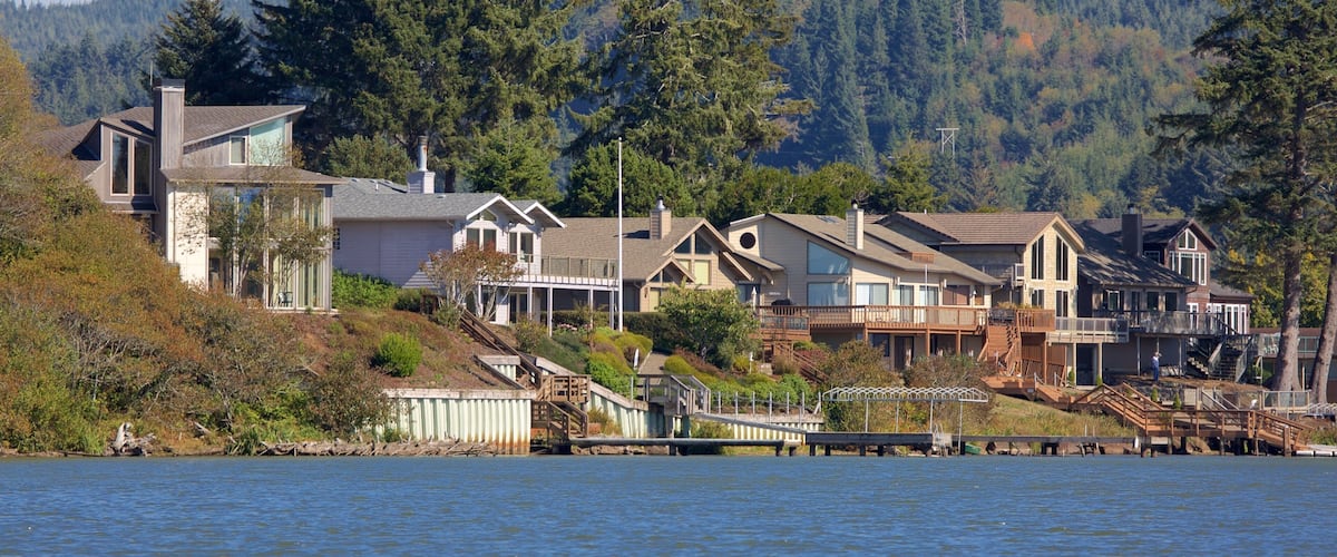 A waterfront residential area with houses, a dock, and a forested hillside.
