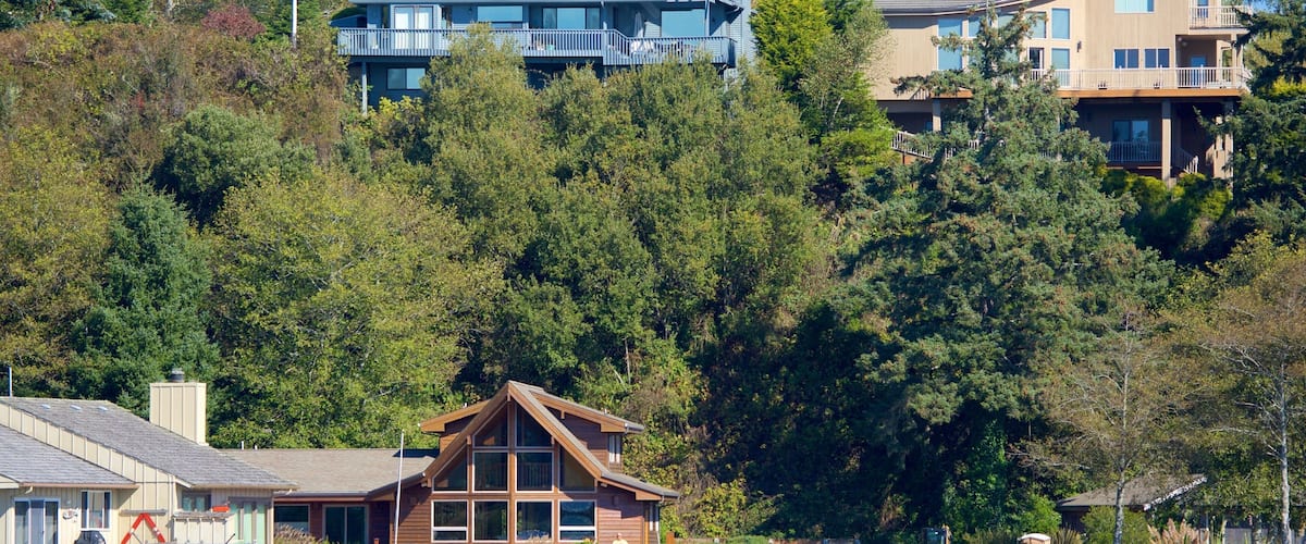 A wooden cabin by a lake with a boat docked nearby.