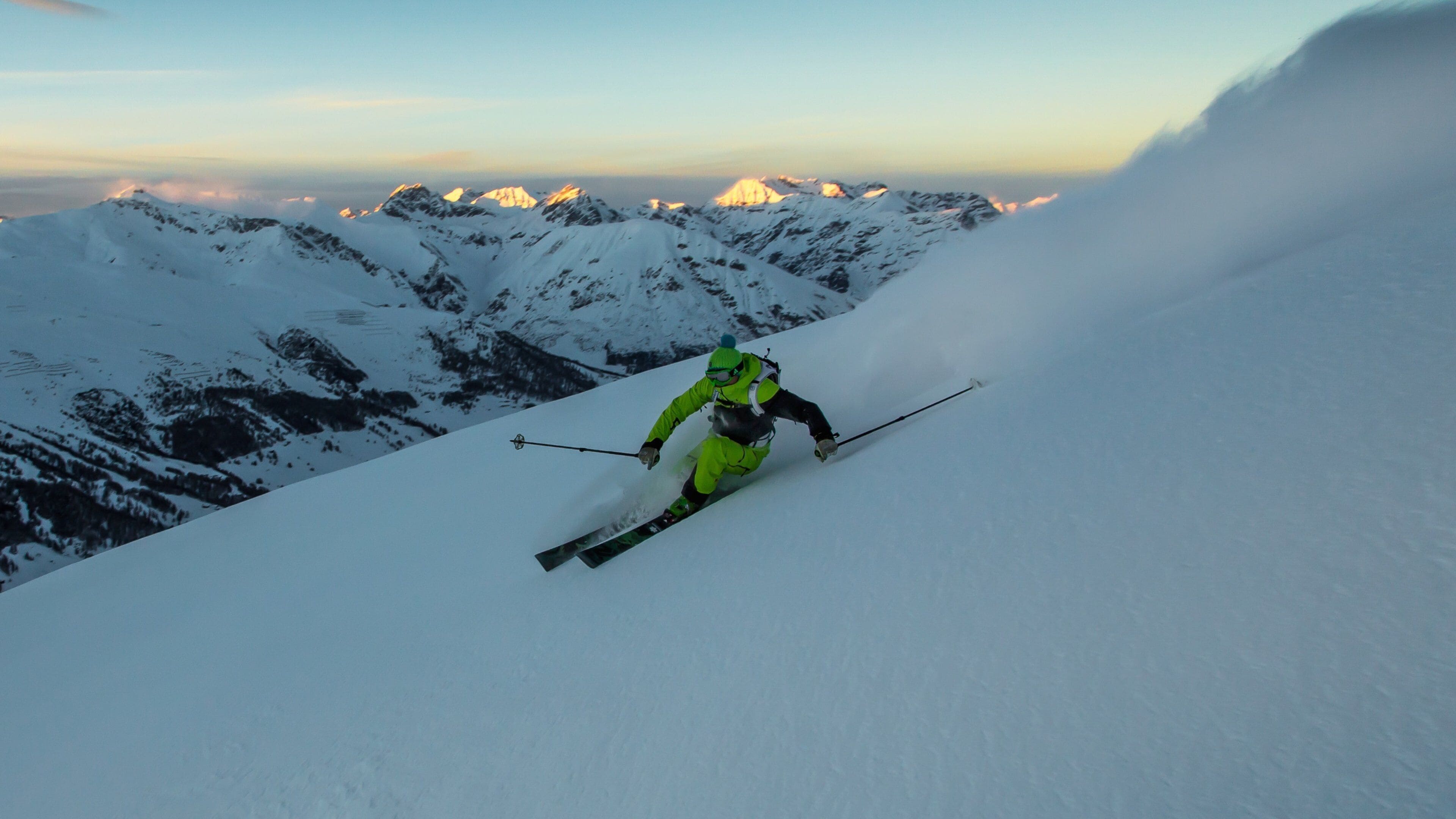 A skier descending a snow-covered slope with a mountainous backdrop.