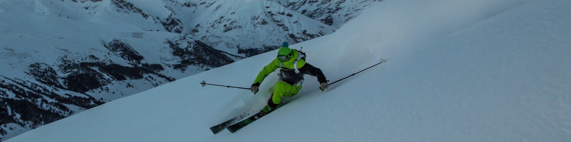 A skier descending a snow-covered slope with a mountainous backdrop.