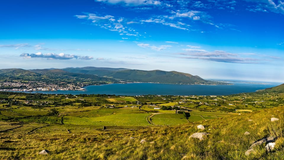 A coastal landscape with rolling hills, a lake, and a town in the distance.