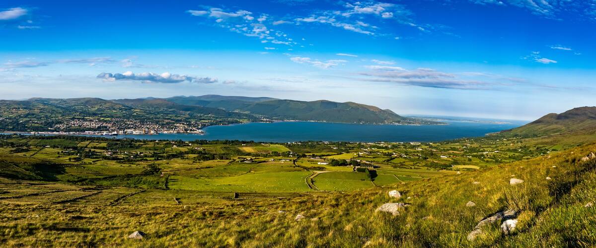 A coastal landscape with rolling hills, a lake, and a town in the distance.