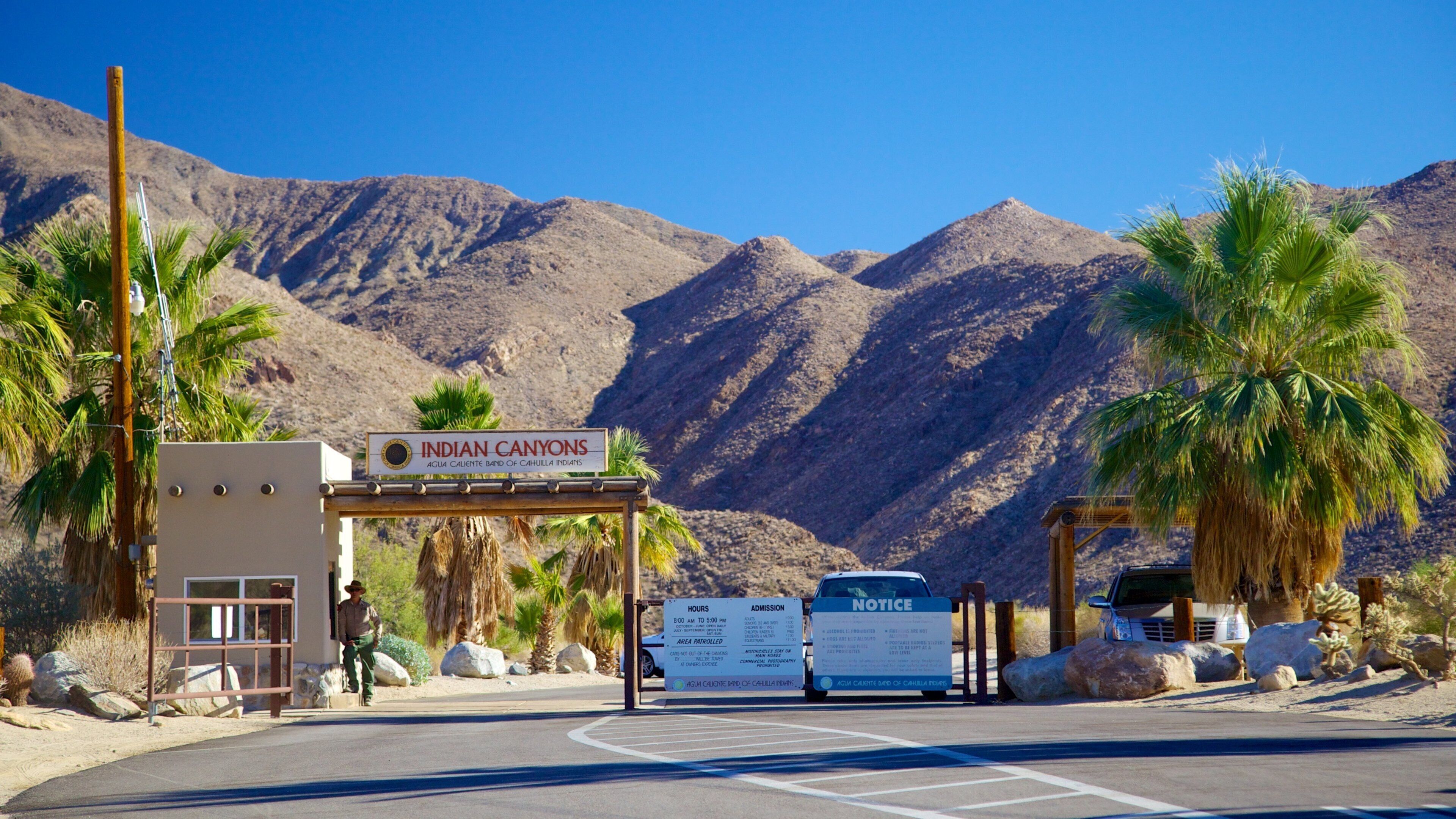 The Indian Canyons entrance with a sign, a man standing, and a notice board.