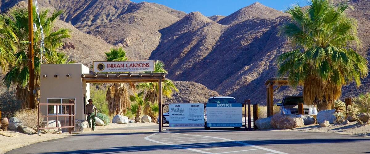 The Indian Canyons entrance with a sign, a man standing, and a notice board.