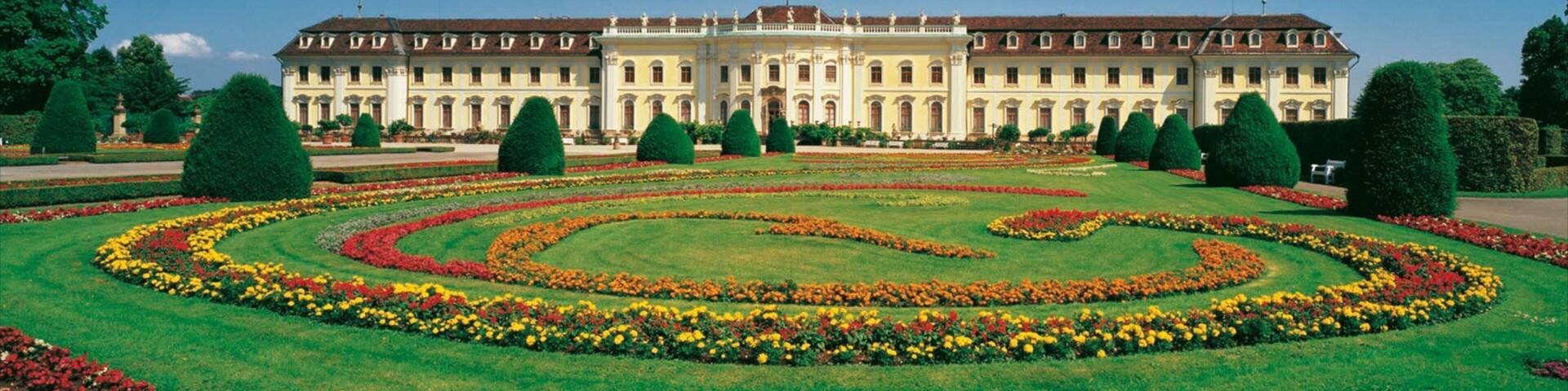 A grand building with symmetrical gardens and manicured lawns.