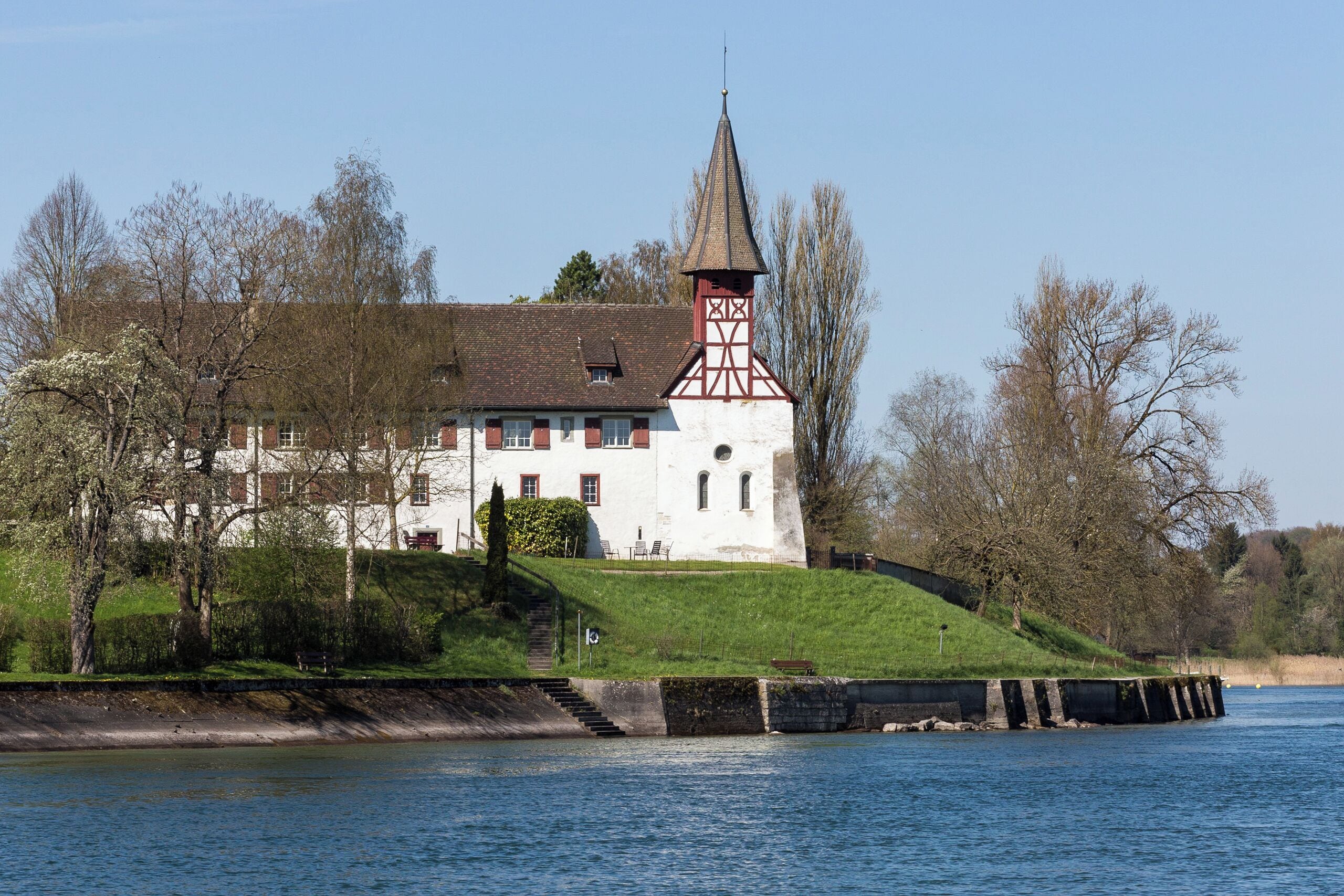 A white building with a red tower by a river.