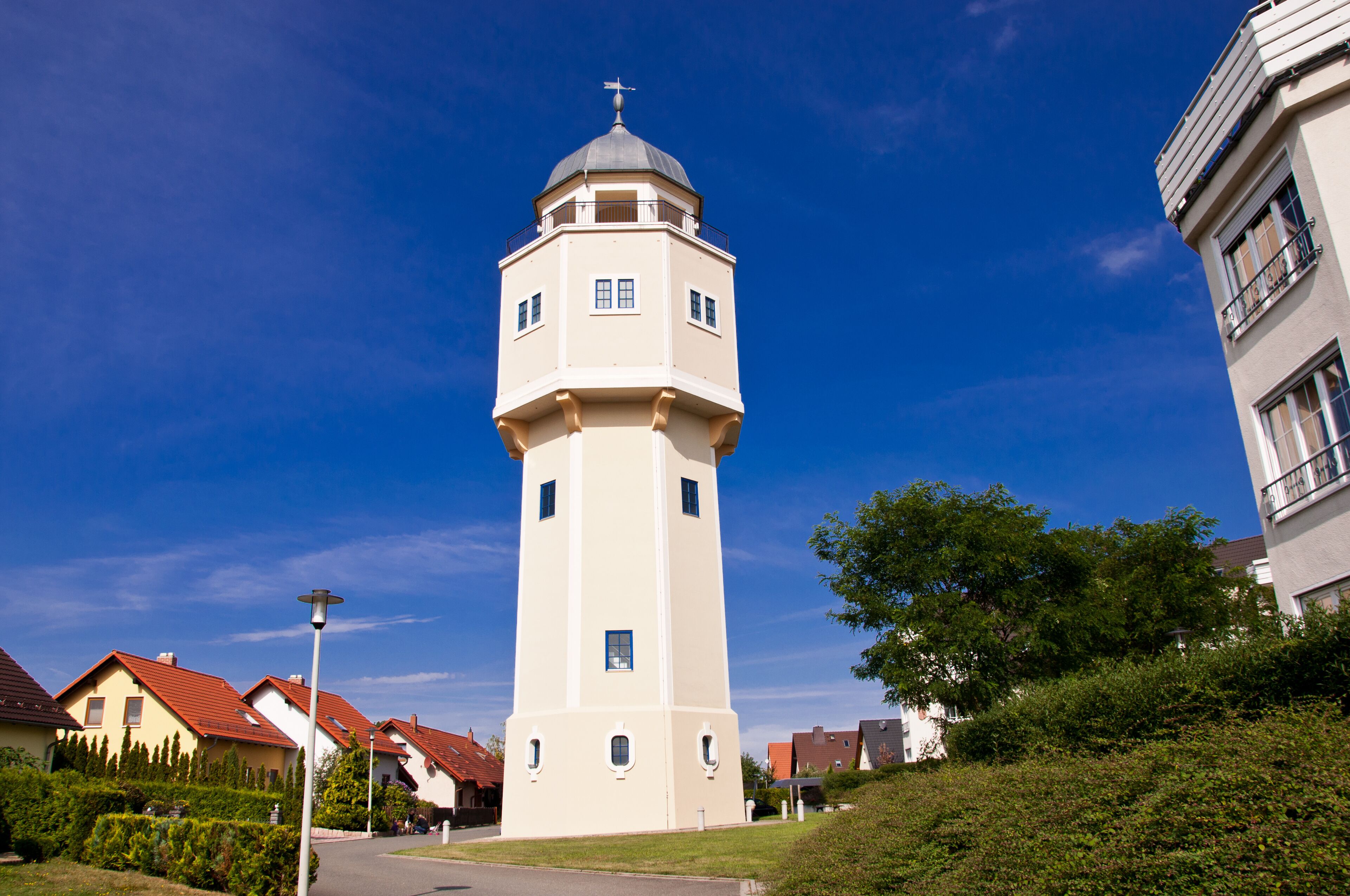 A white tower with a dome and a cross on top, surrounded by houses with red roofs and greenery.